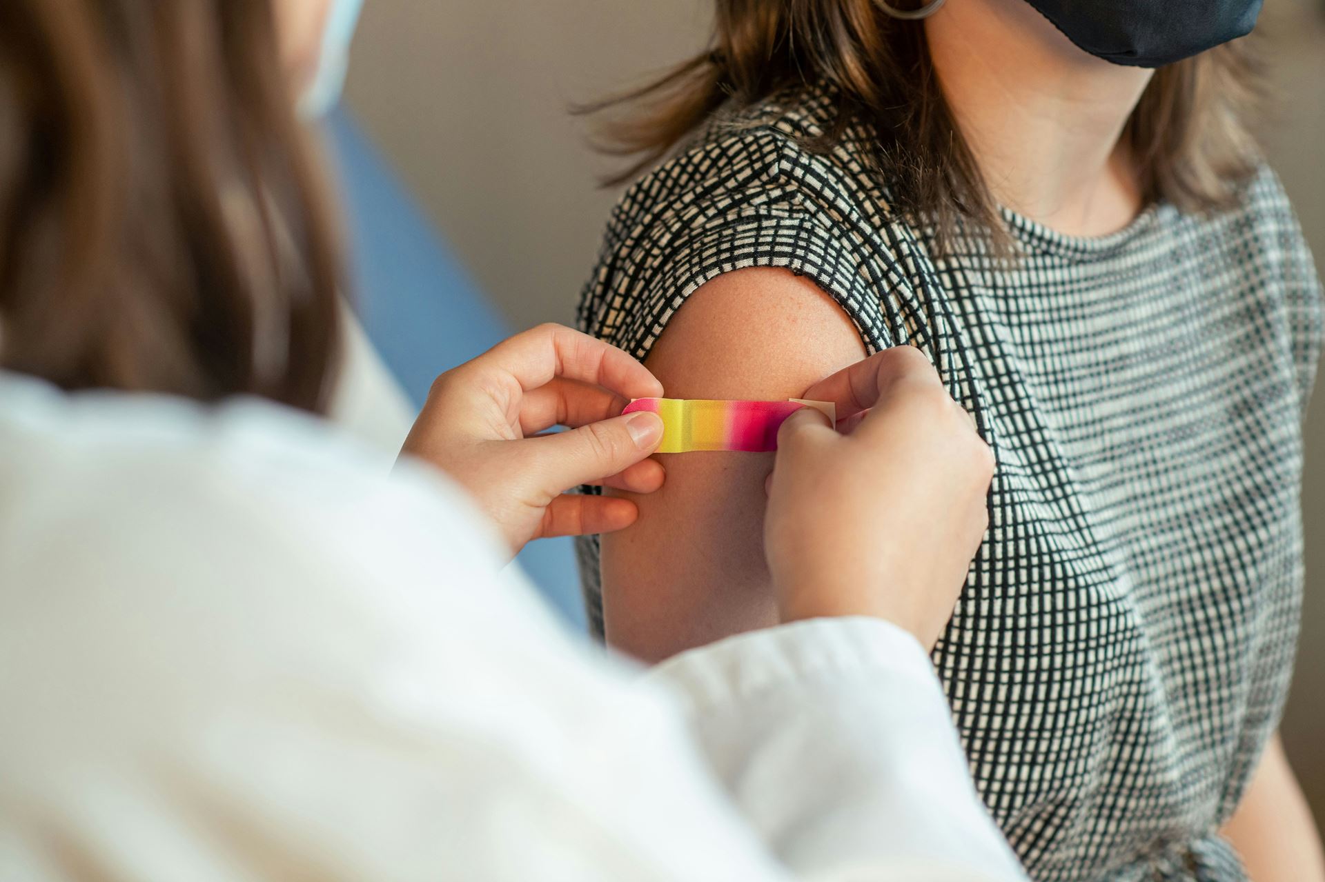 Picture of a clinician putting a plaster on the upper arm of a woman who has just been given a flu vaccination